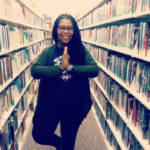 Amanda M. Leftwich is standing between two rows of bookshelves in a library. She is doing a yoga pose that inspires mindfulness.